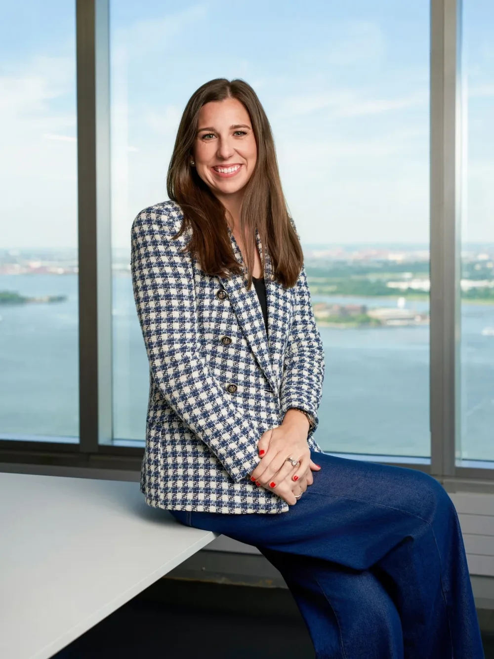 Woman in a checked jacket seated beside large office windows.