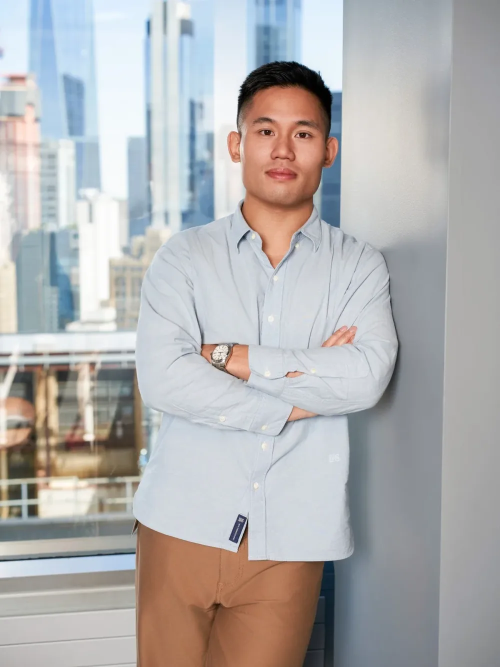 Man in a light blue shirt standing beside office windows.