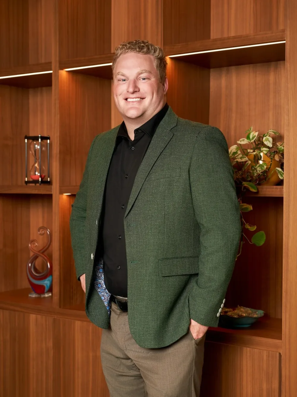 Man in a green jacket standing in front of wood-paneled shelves.