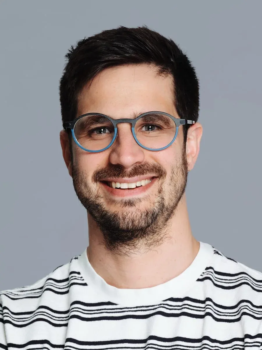 Man in blue glasses and a striped shirt against a grey background.