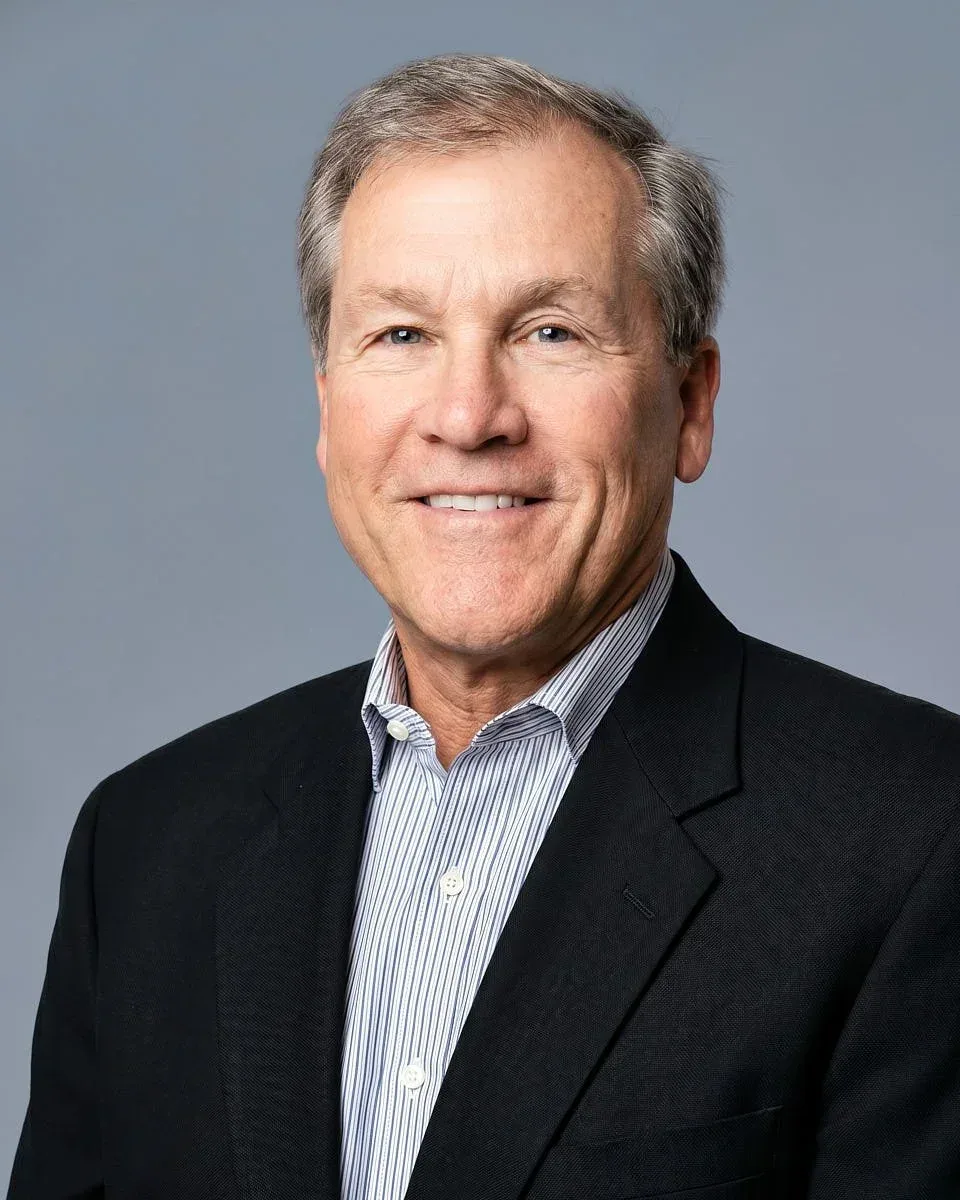 Man in a dark blazer against a grey background.