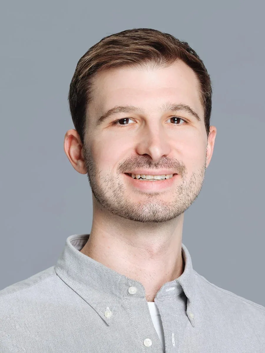 Man in a light grey button-down shirt against a grey background.