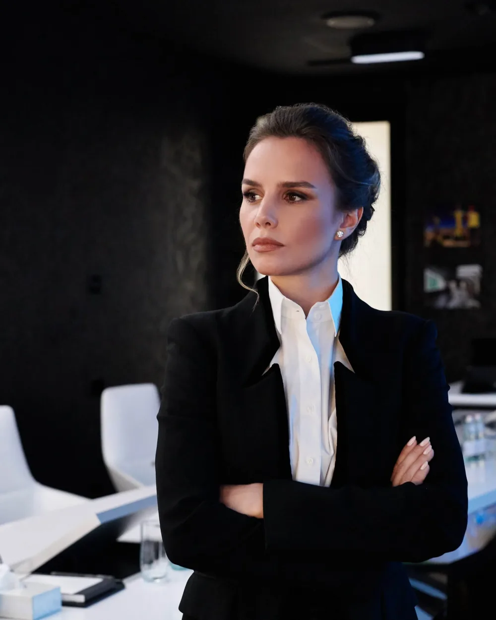 Woman in a black blazer and white shirt standing beside a conference table.