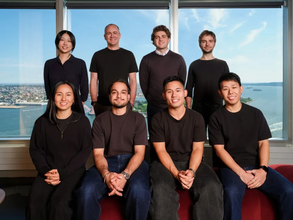 Group portrait in two rows beside office windows overlooking the city.