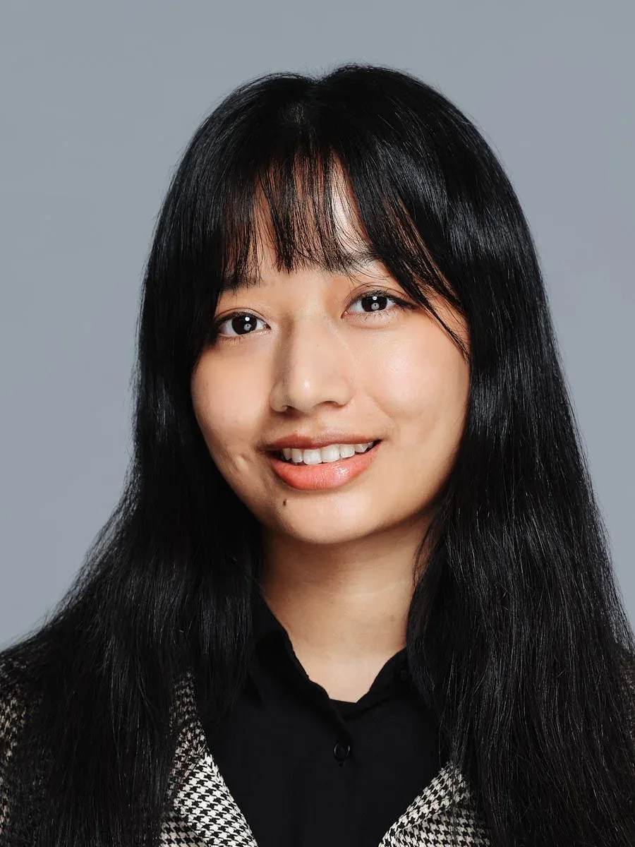 Woman with dark hair and bangs in a black collared top against a grey background.