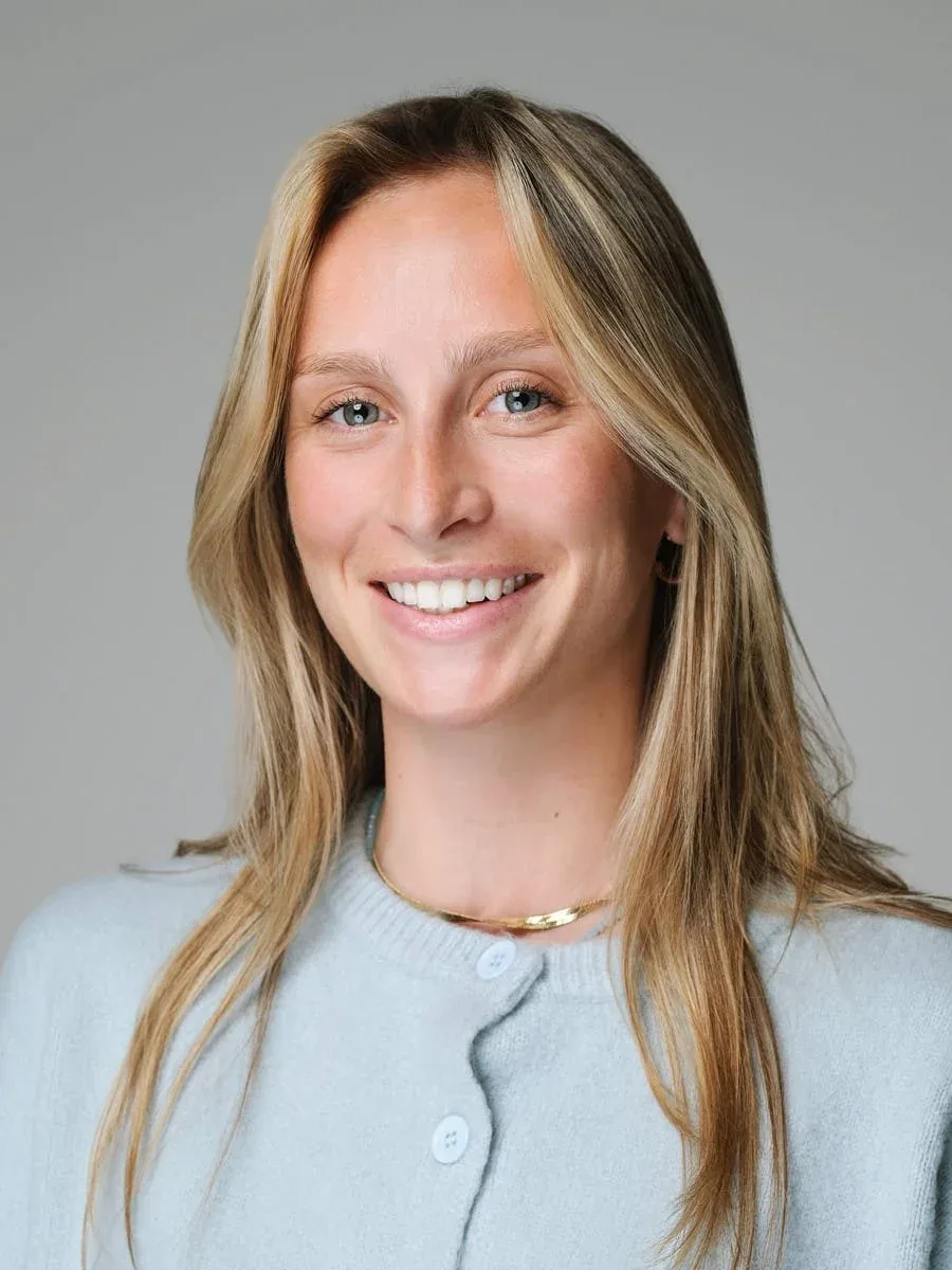 Woman in a light blue cardigan against a grey background.