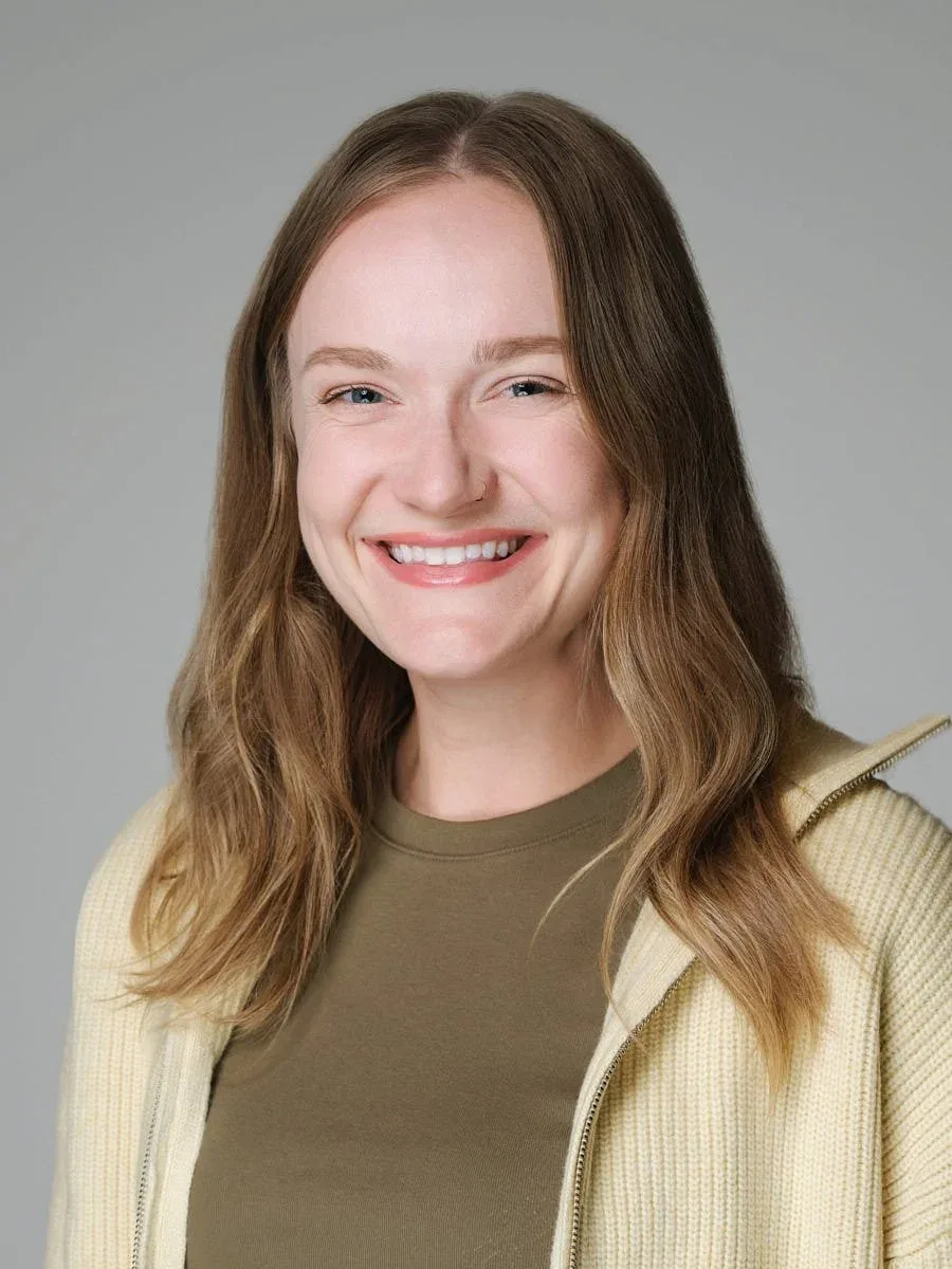 Woman in an olive top and cream cardigan against a grey background.
