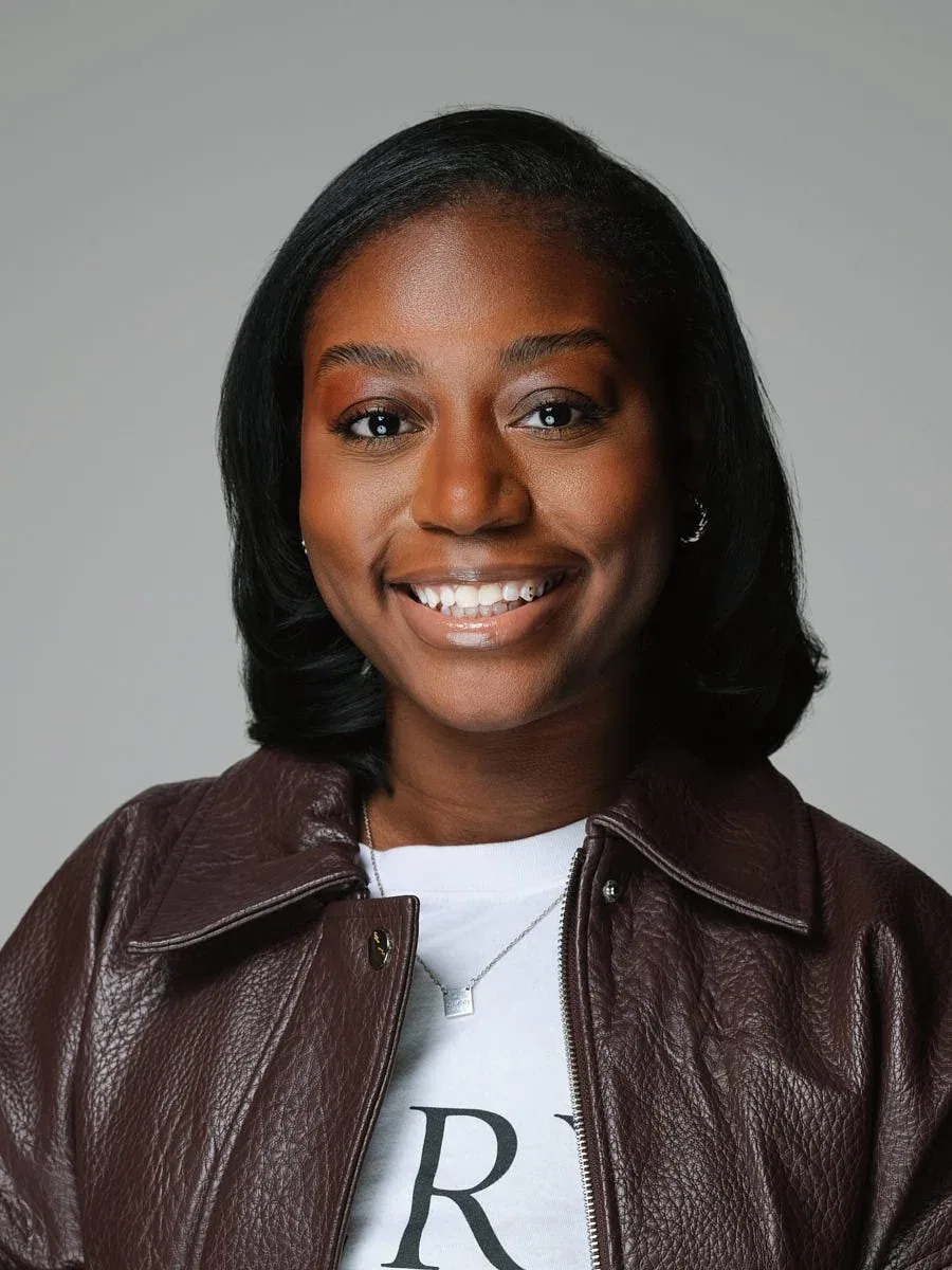 Woman in a brown leather jacket against a grey background.