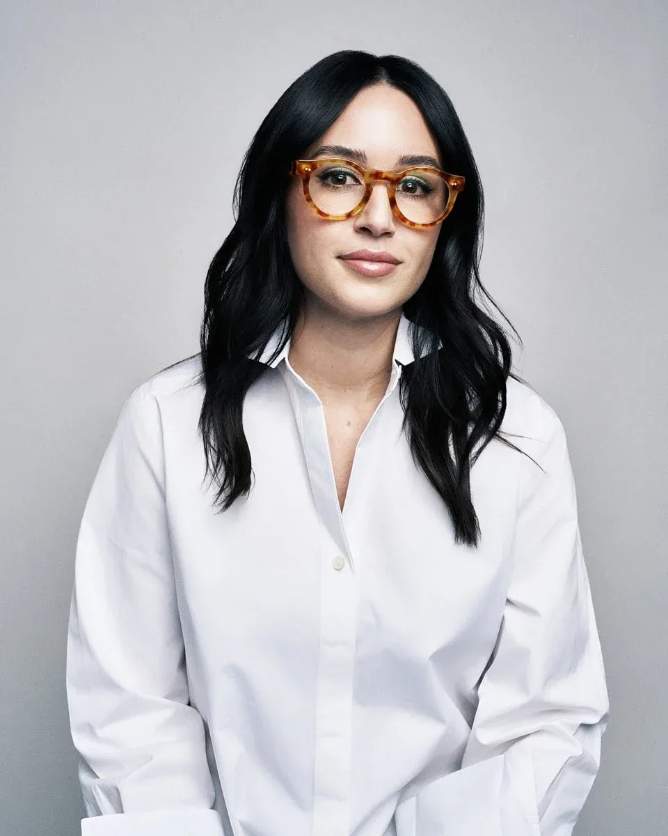 Woman in glasses and a white shirt against a pale background.
