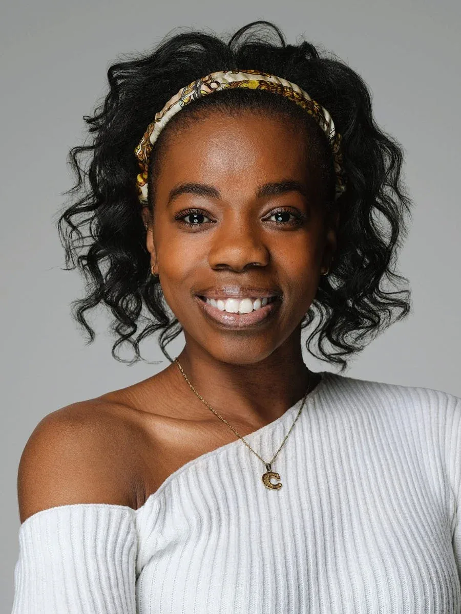 Woman in a white top and patterned headband against a grey background.