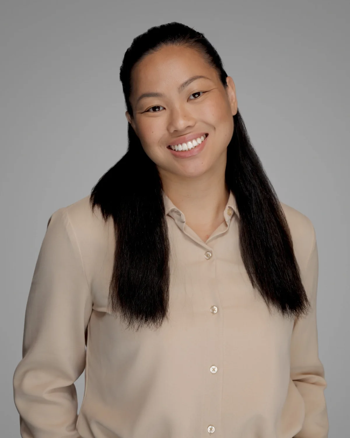 A person in a light blouse, centered against a gray backdrop.