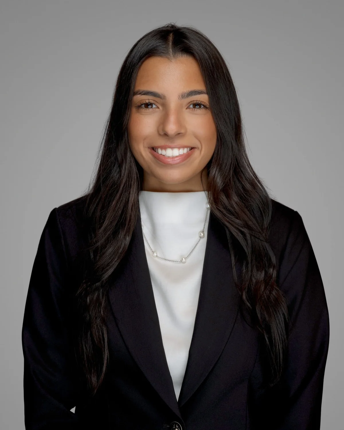 A person in a dark blazer over a white top, centered against a gray studio backdrop.